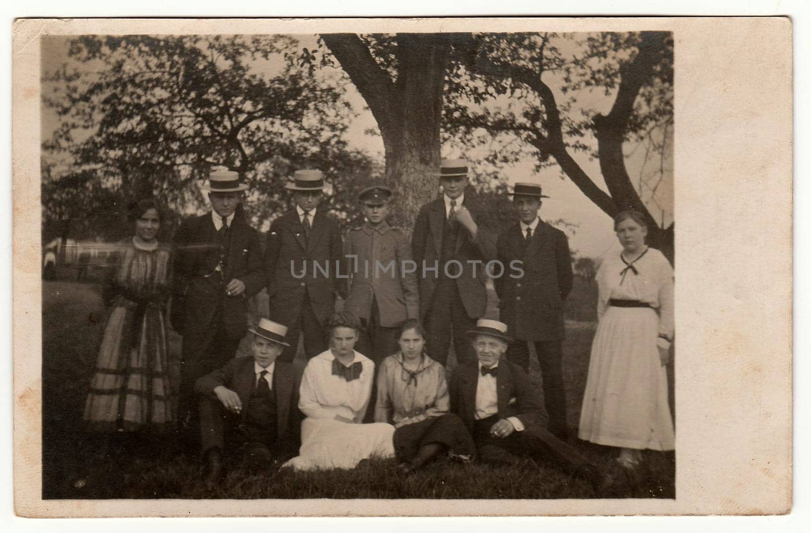 Vintage photo shows young people pose outdoors. Men wear wide-brimmed hat with band and dark suit. Black white antique photography. by roman_nerud