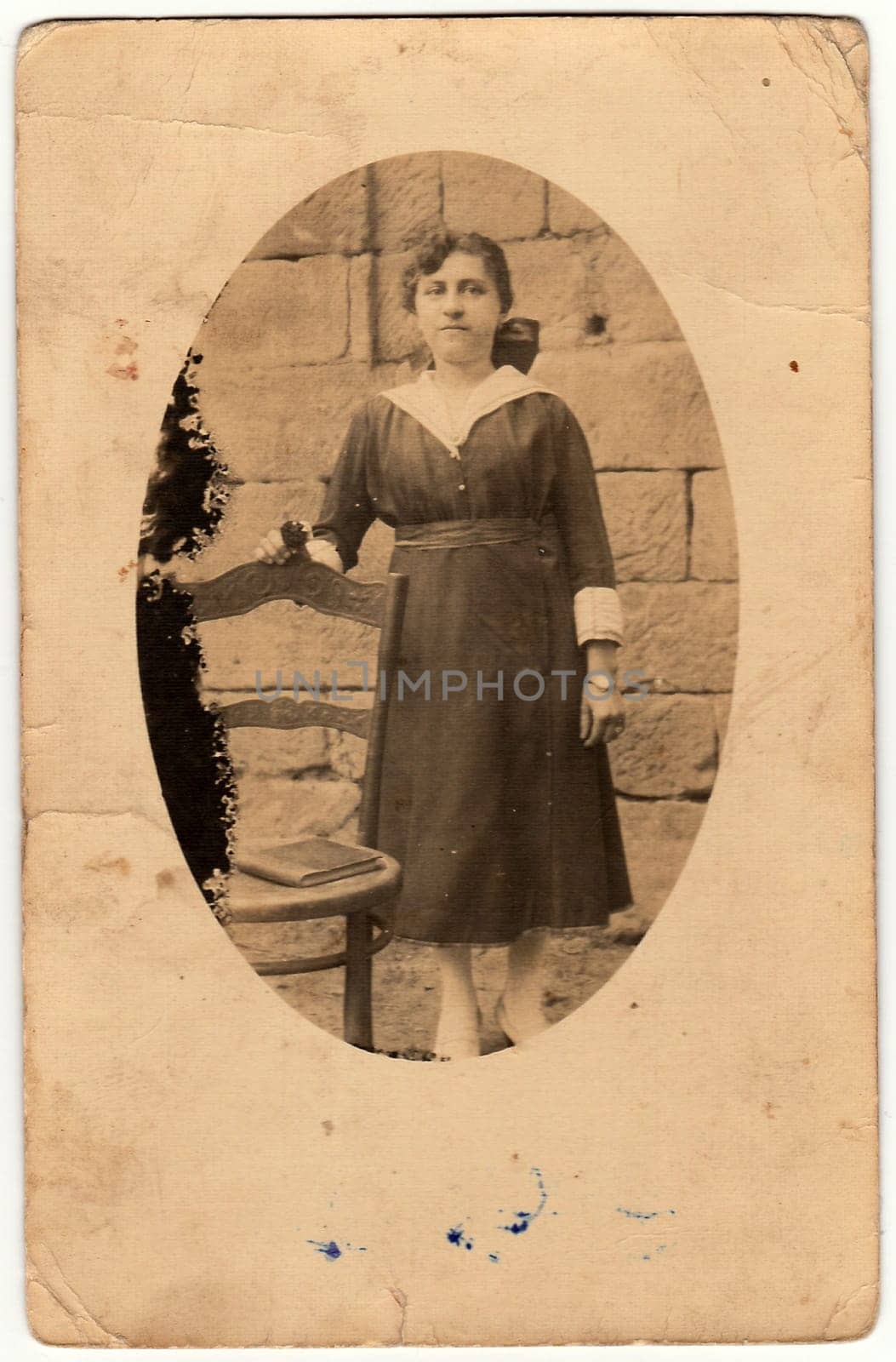 Vintage photo shows woman poses next to historic chair. Antique black white photo is oval shaped. by roman_nerud