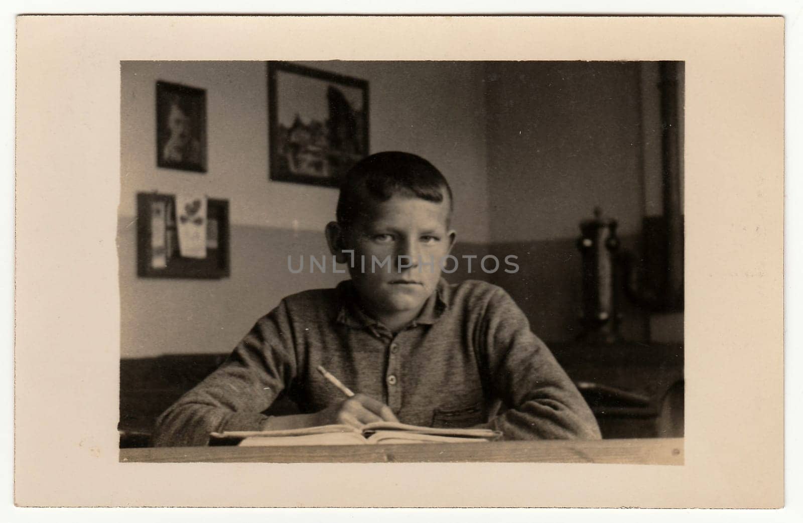 EILENBURG, GERMANY - CIRCA 1940s: Vintage photo shows young boy (pupil, student) sits at the classroom. Black white antique photography.