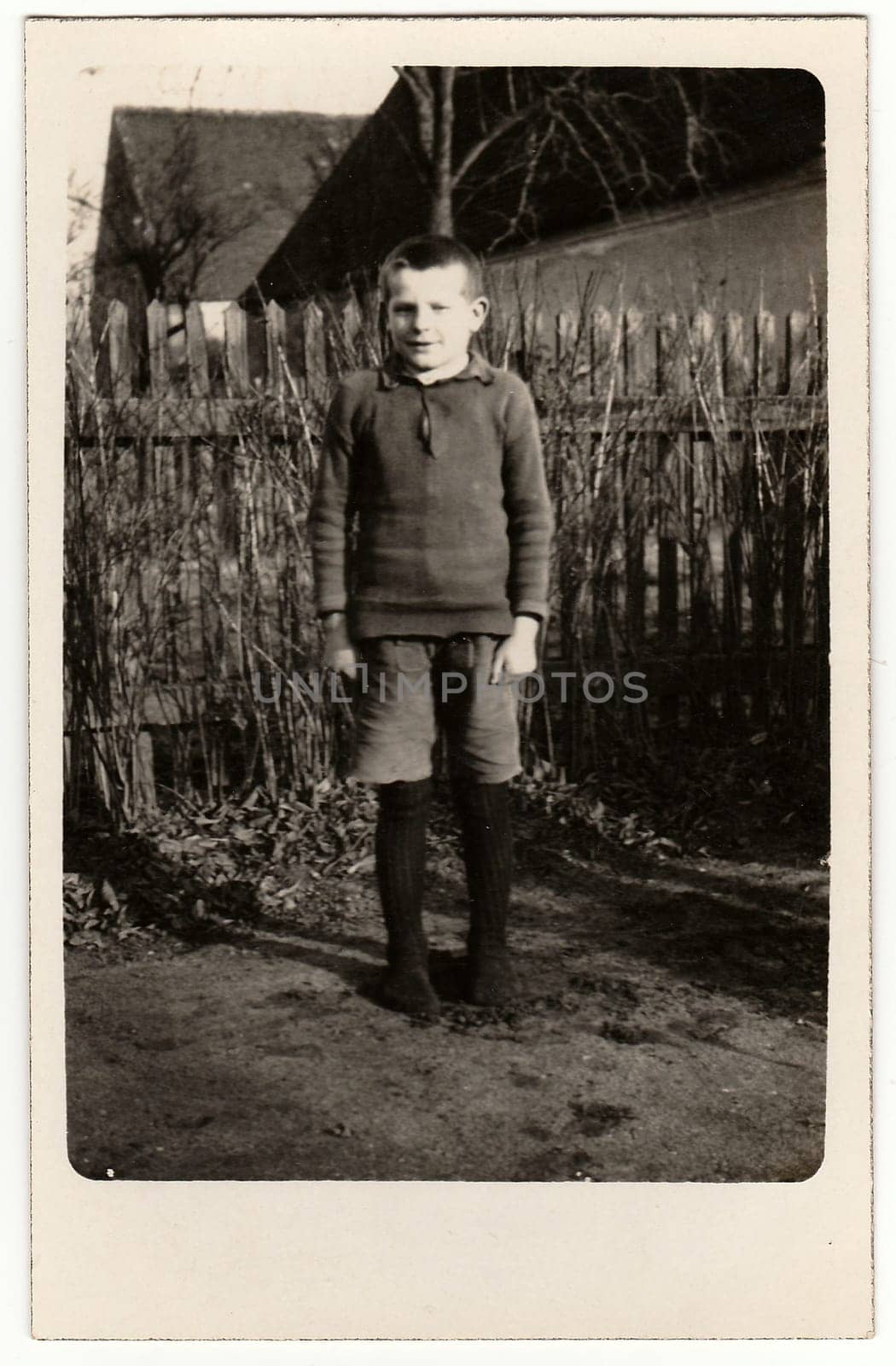 Vintage photo shows young boy pupil, student stands in front of wooden fence. Black white antique photography by roman_nerud