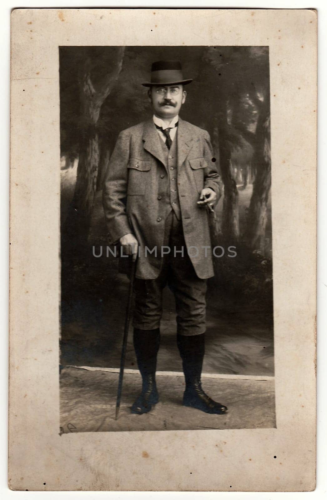 Vintage photo shows man gamekeeper poses with walking stick and cigar in the photography studio. Black white antique photo. by roman_nerud