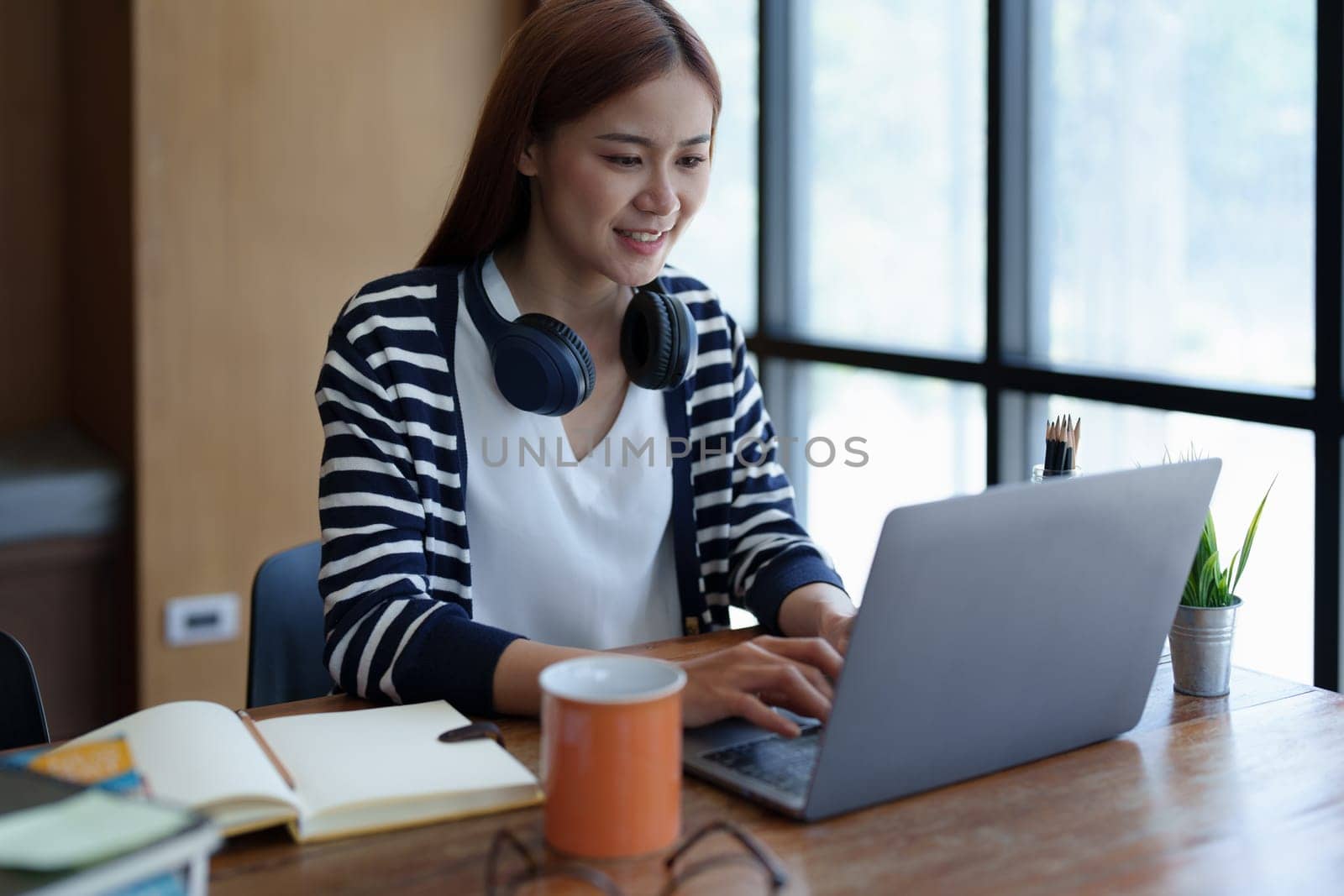 Portrait of a young, attractive Asian teenage girl using a computer and drinking coffee while studying online in the morning at the library by Manastrong