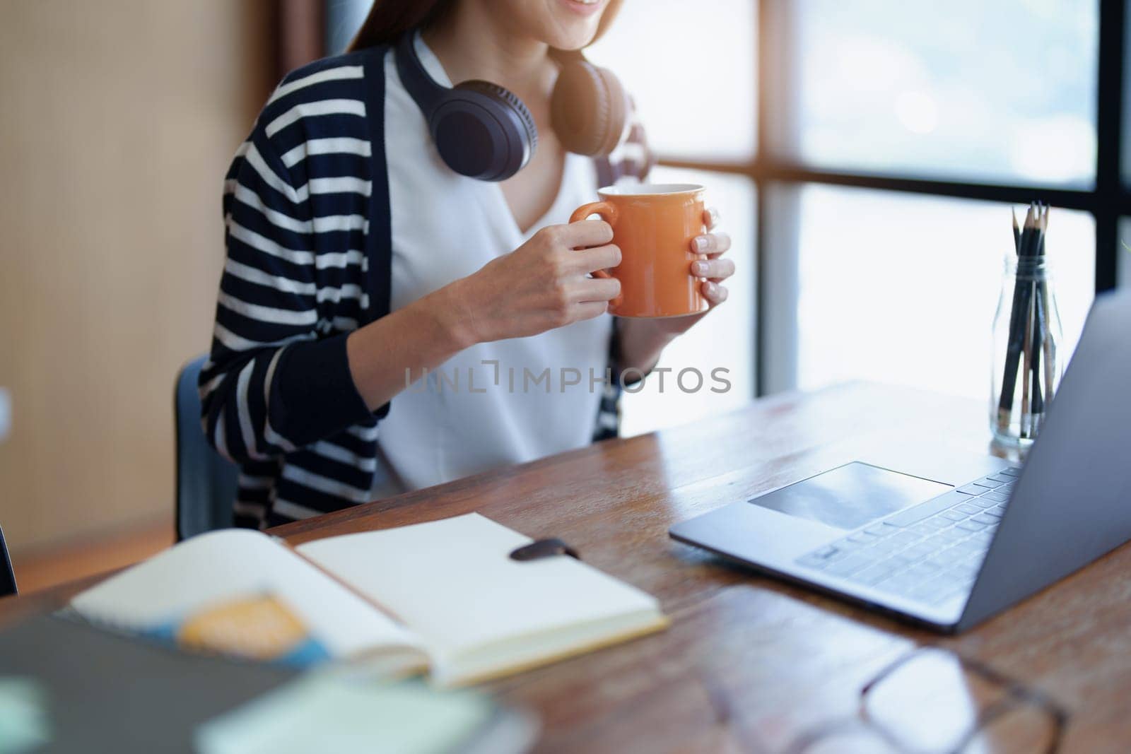 Portrait of a young, attractive Asian teenage girl using a computer and drinking coffee while studying online in the morning at the library.