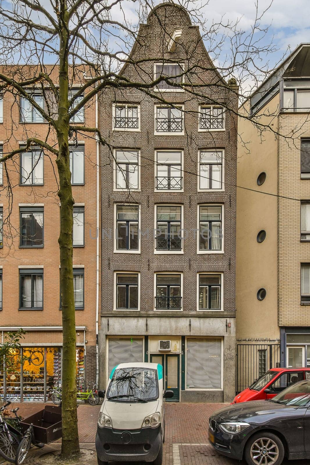 two cars parked on the side of a street in front of an apartment building and a tree with no leaves