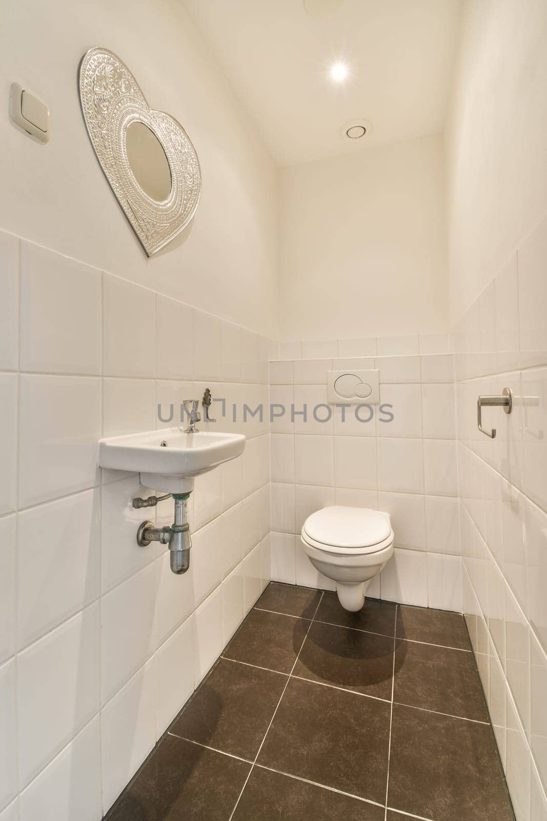 a bathroom with white tiles and black flooring on the walls, there is a mirror above the toilet bowl