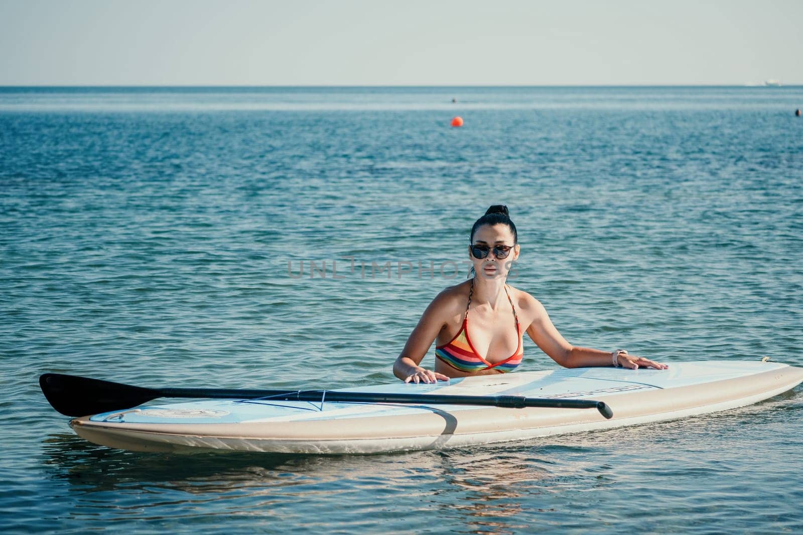 Sea woman sup. Silhouette of happy middle aged woman in rainbow bikini, surfing on SUP board, confident paddling through water surface. Idyllic sunset. Active lifestyle at sea or river