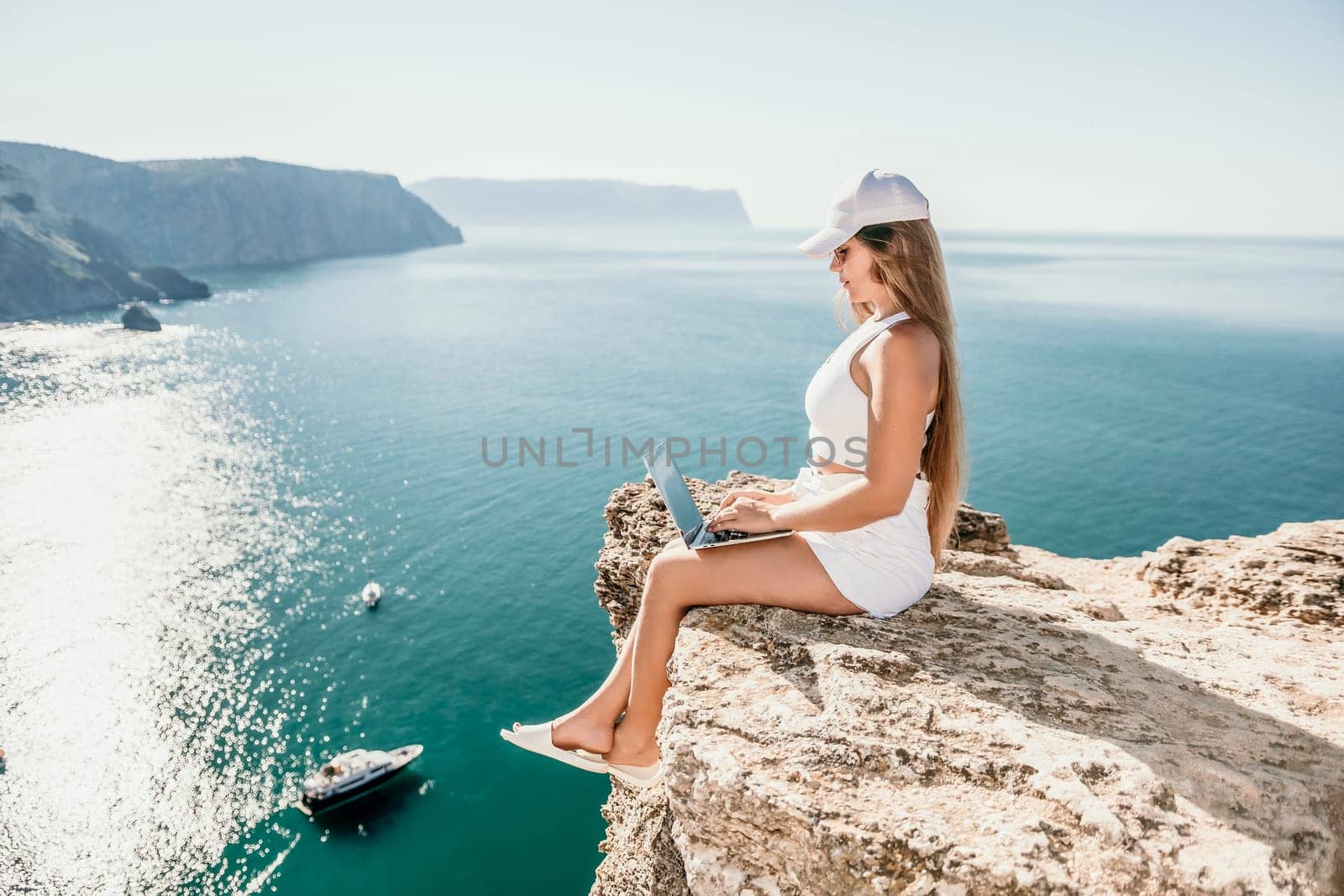 Digital nomad, Business woman working on laptop by the sea. Pretty lady typing on computer by the sea at sunset, makes a business transaction online from a distance. Freelance, remote work on vacation by panophotograph