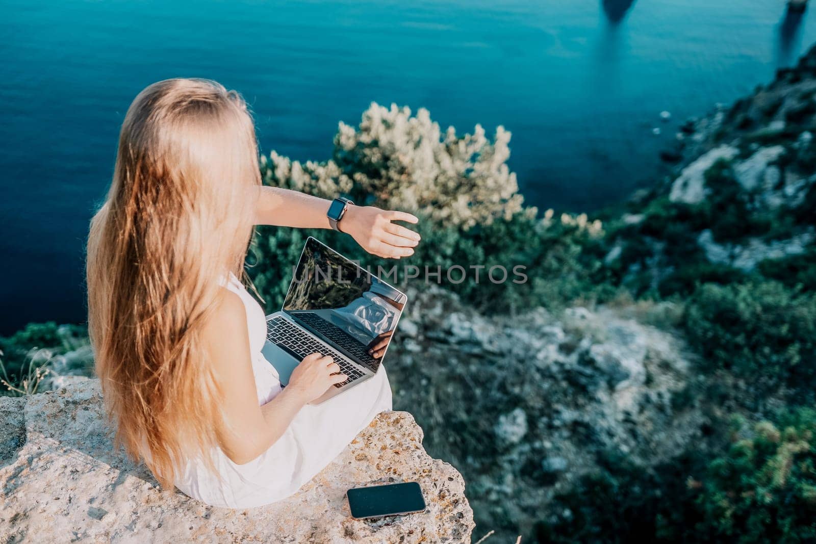 Digital nomad, Business woman working on laptop by the sea. Pretty lady typing on computer by the sea at sunset, makes a business transaction online from a distance. Freelance, remote work on vacation by panophotograph