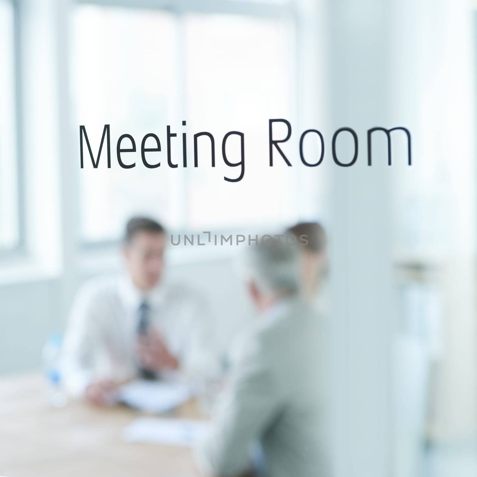 Behind closed doors. Closeup of a glass door reading meeting room with business people blurred in the room behind