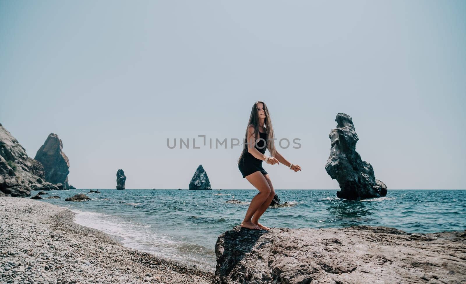 Woman travel sea. Young Happy woman in a long red dress posing on a beach near the sea on background of volcanic rocks, like in Iceland, sharing travel adventure journey