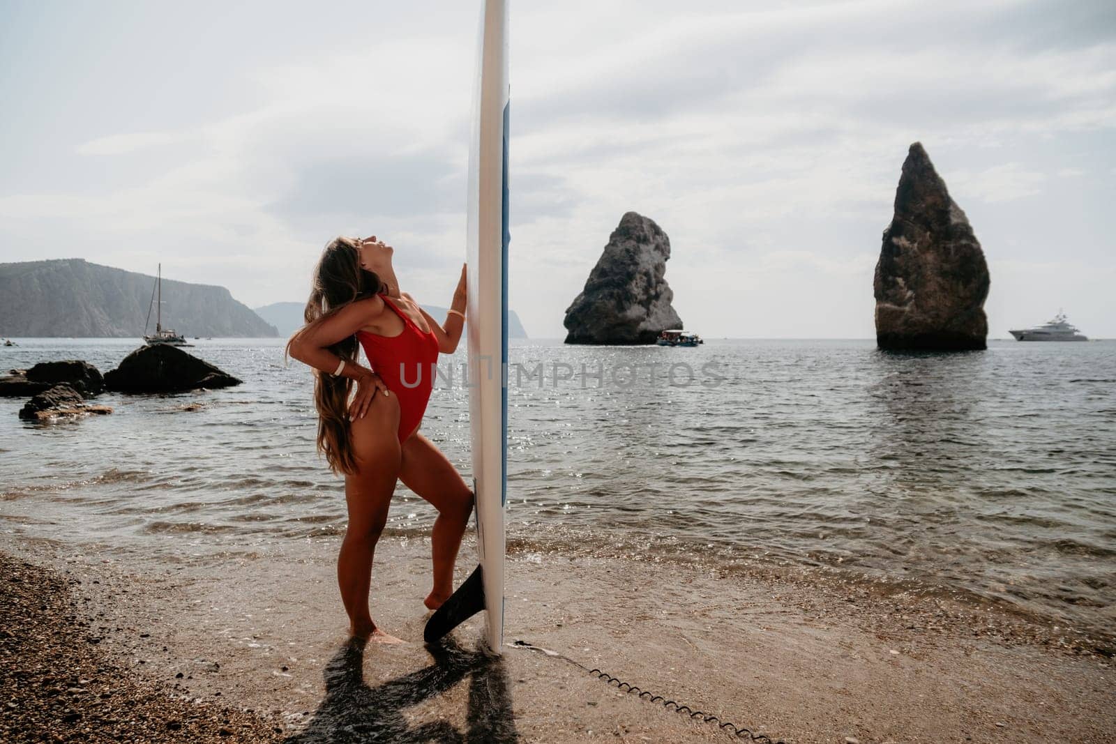 Close up shot of beautiful young caucasian woman with black hair and freckles looking at camera and smiling. Cute woman portrait in a pink bikini posing on a volcanic rock high above the sea