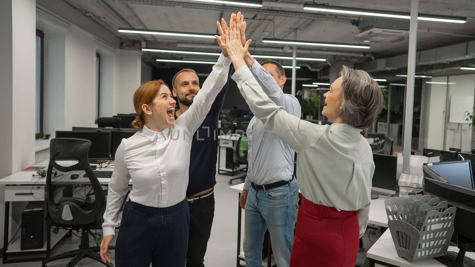 Four co-workers give a high five in the office. by mrwed54