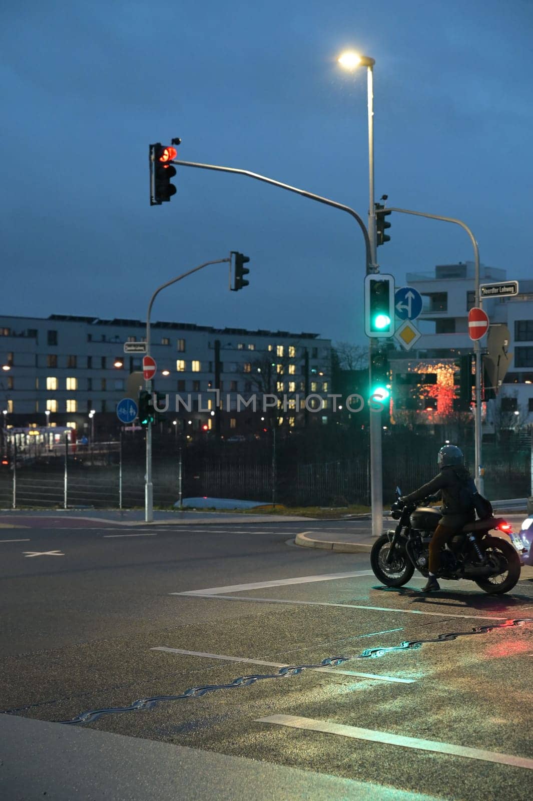 Motorcyclist with retro motorcycle standing in front of a green traffic light in Heerdt