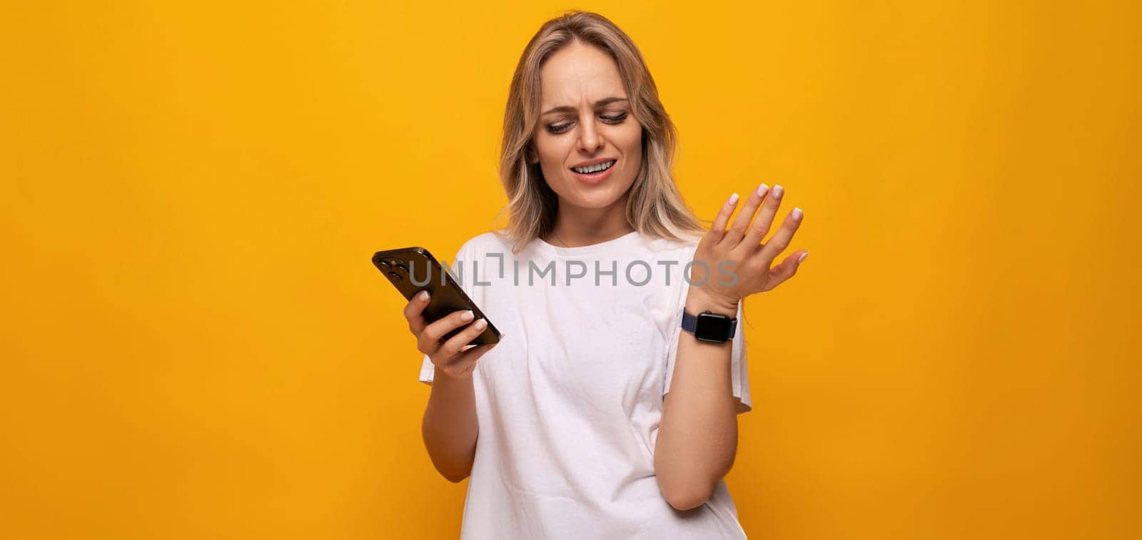 a woman in a white T-shirt with a smartphone in her hands uses an application on a yellow background by TRMK