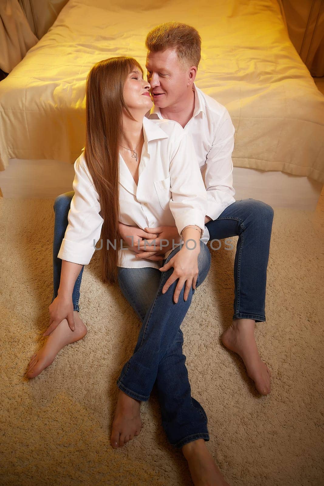 An adult couple of newlyweds in in white shirts in a hotel room after the wedding. A guy and a girl, a man and a woman in a beautiful room. The concept of love and care by keleny