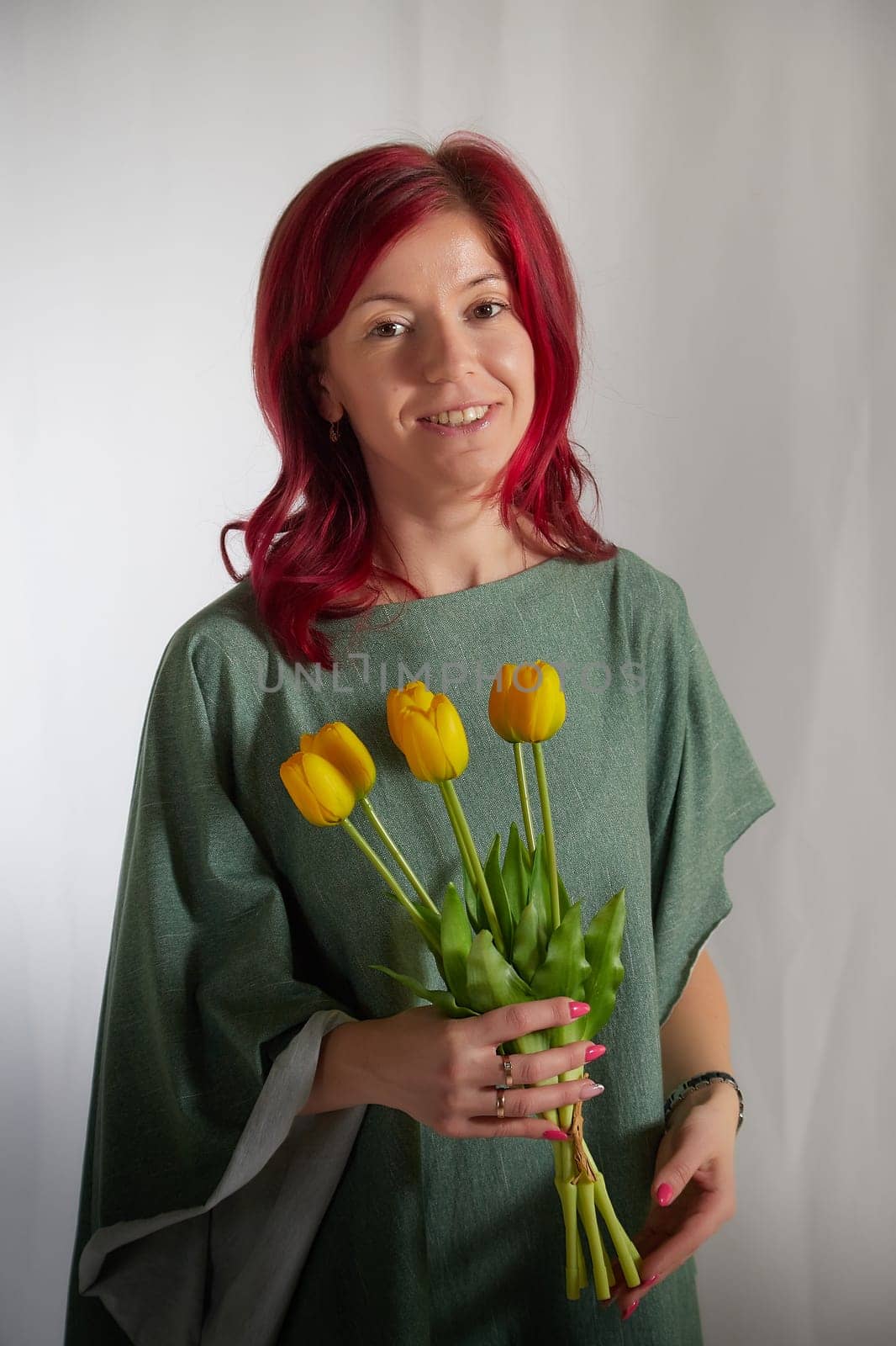 Beautiful woman with red hair in yellow dress on light background holds tulips. Inernational woman's day 8 March