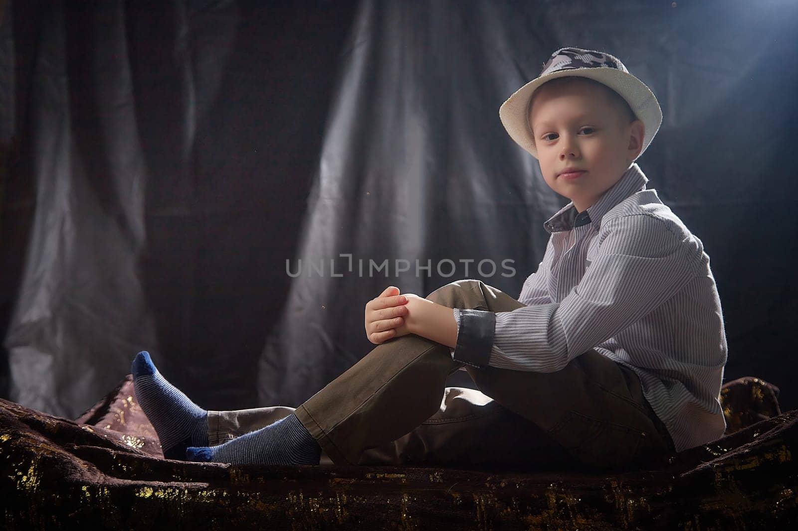 Stylish and fashionable young boy in a shirt and hat in the studio on a black fabric background with flashes. Contour portrait of a male model by keleny