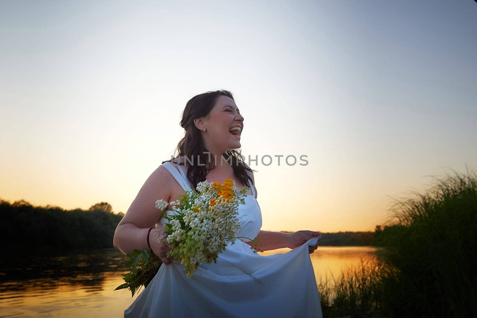 Slavic plump plump chubby girl in long white dress on the feast of Ivan Kupala with flowers and water in a river or lake on a summer evening by keleny