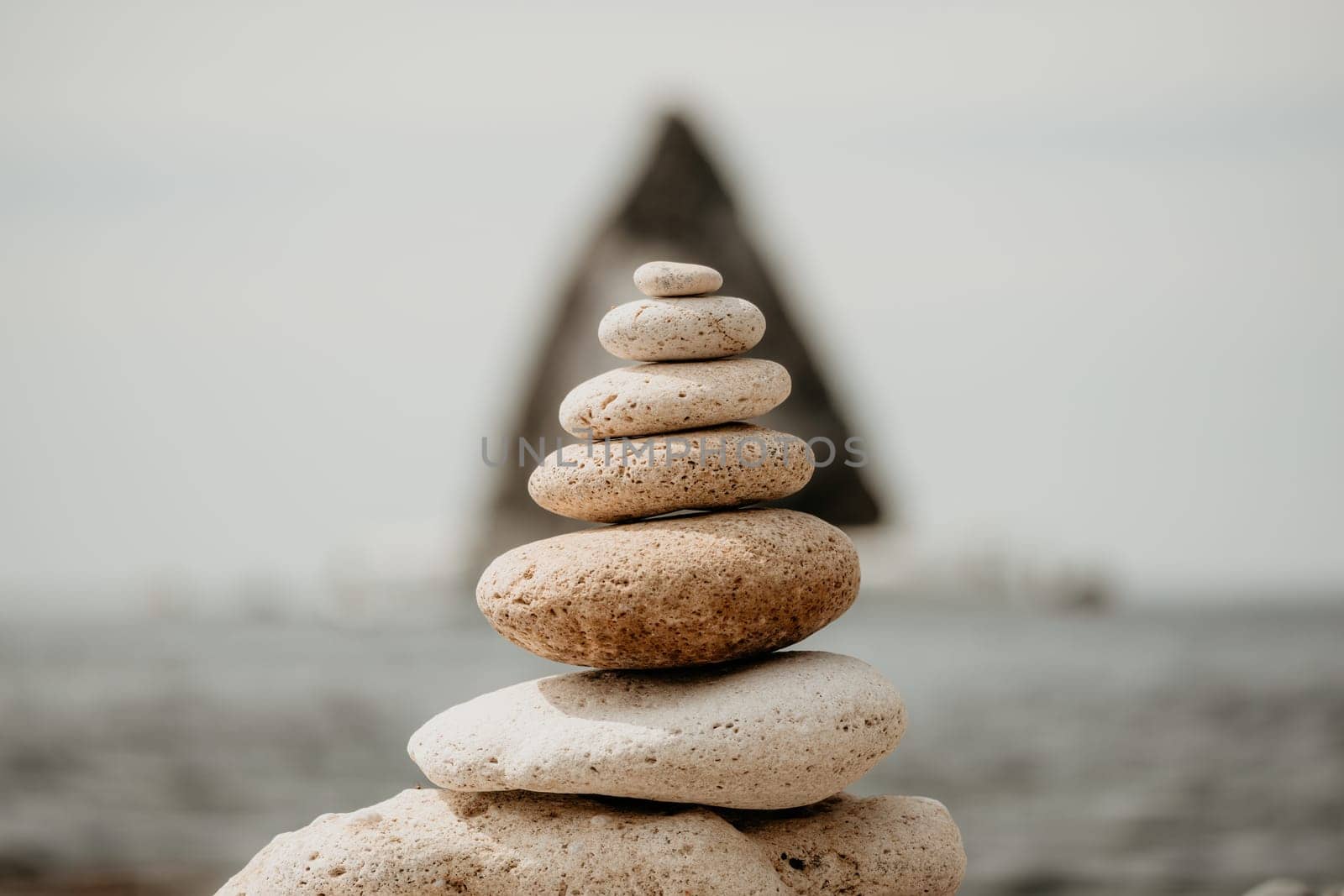 Pyramid stones on the seashore with warm sunset on the sea background. Happy holidays. Pebble beach, calm sea, travel destination. Concept of happy vacation on the sea, meditation, spa, calmness.