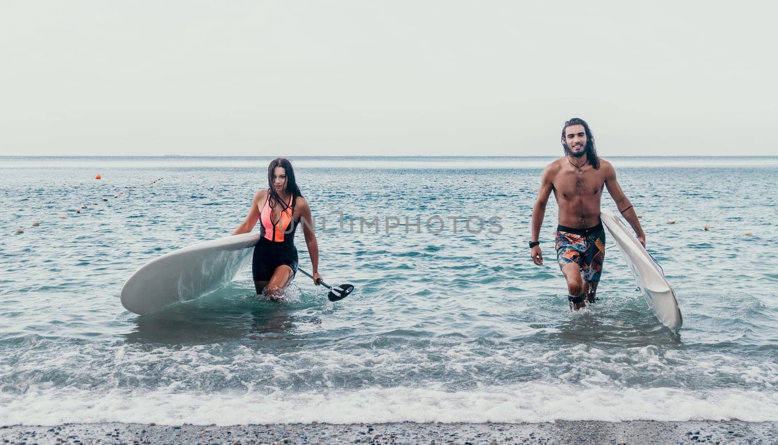 Sea woman and man on sup. Silhouette of happy young woman and man, surfing on SUP board, confident paddling through water surface. Idyllic sunset. Active lifestyle at sea or river