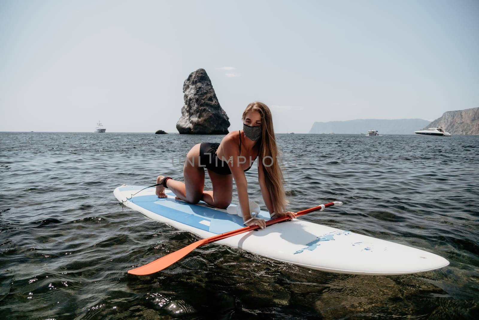 Close up shot of beautiful young caucasian woman with black hair and freckles looking at camera and smiling. Cute woman portrait in a pink bikini posing on a volcanic rock high above the sea