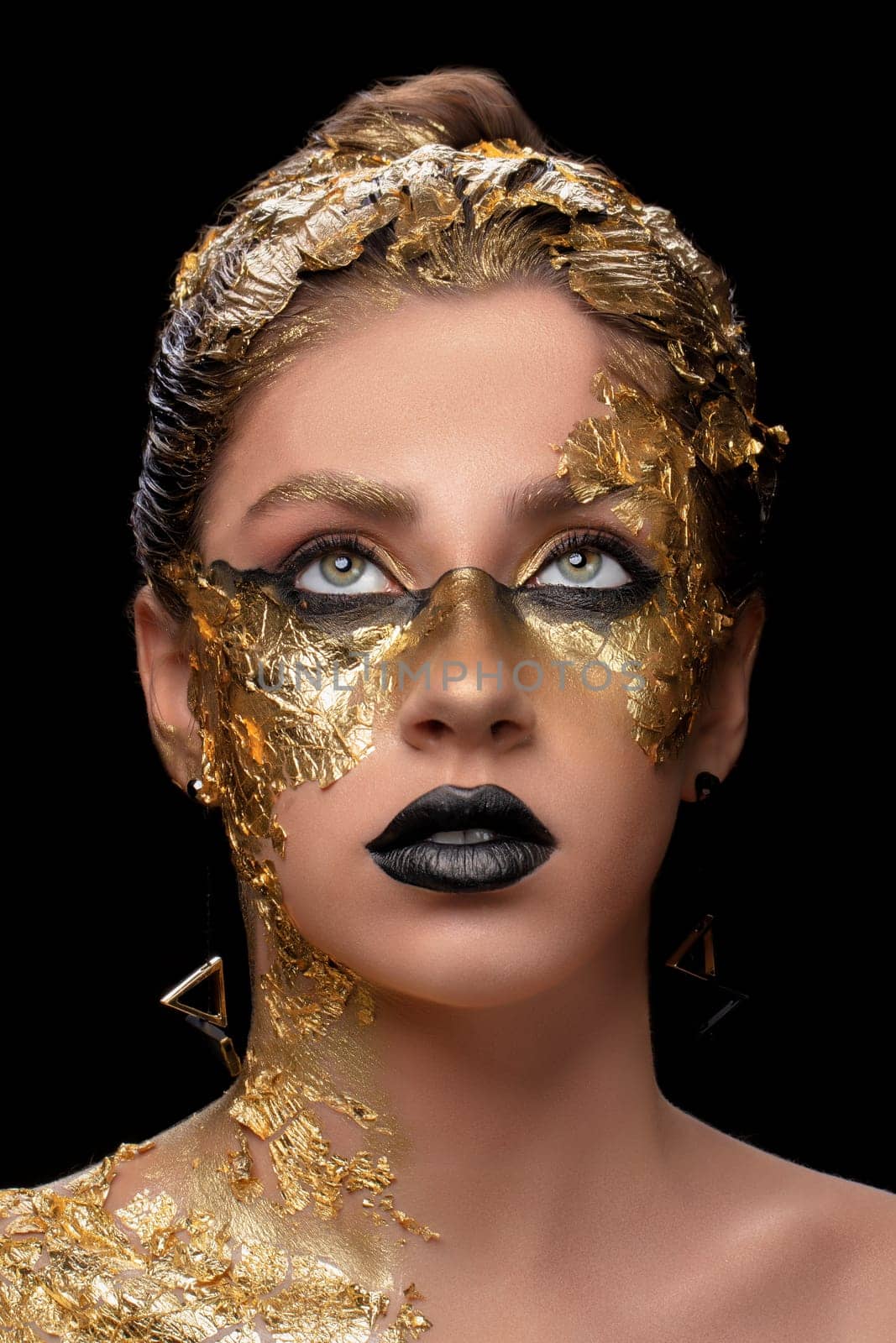 Closeup portrait of beautiful young woman with golden foil on face. Creative golden makeup on black background by Sviatlana