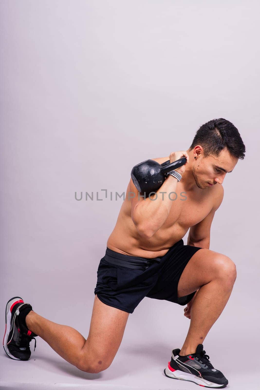 Hispanic male athlete working out with kettlebell on grey background. Crossfit workout theme. by Zelenin