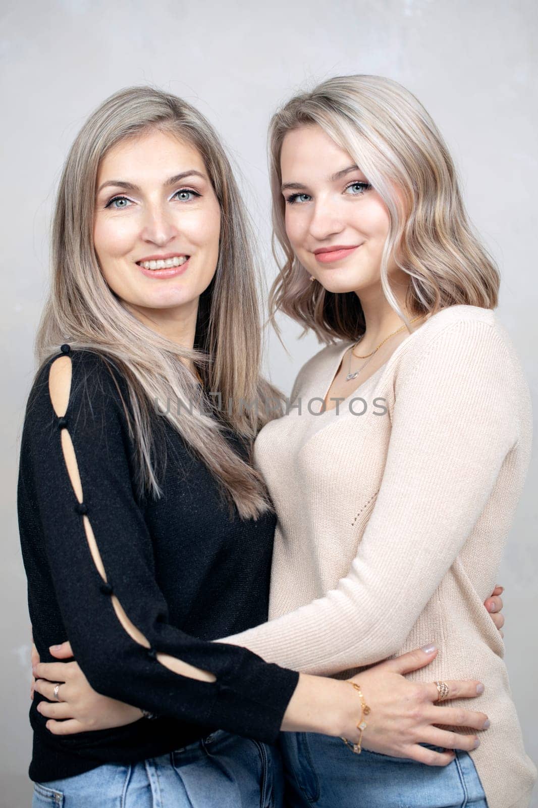 Beautiful middle-aged mother and adult daughter are hugging and looking at the camera.