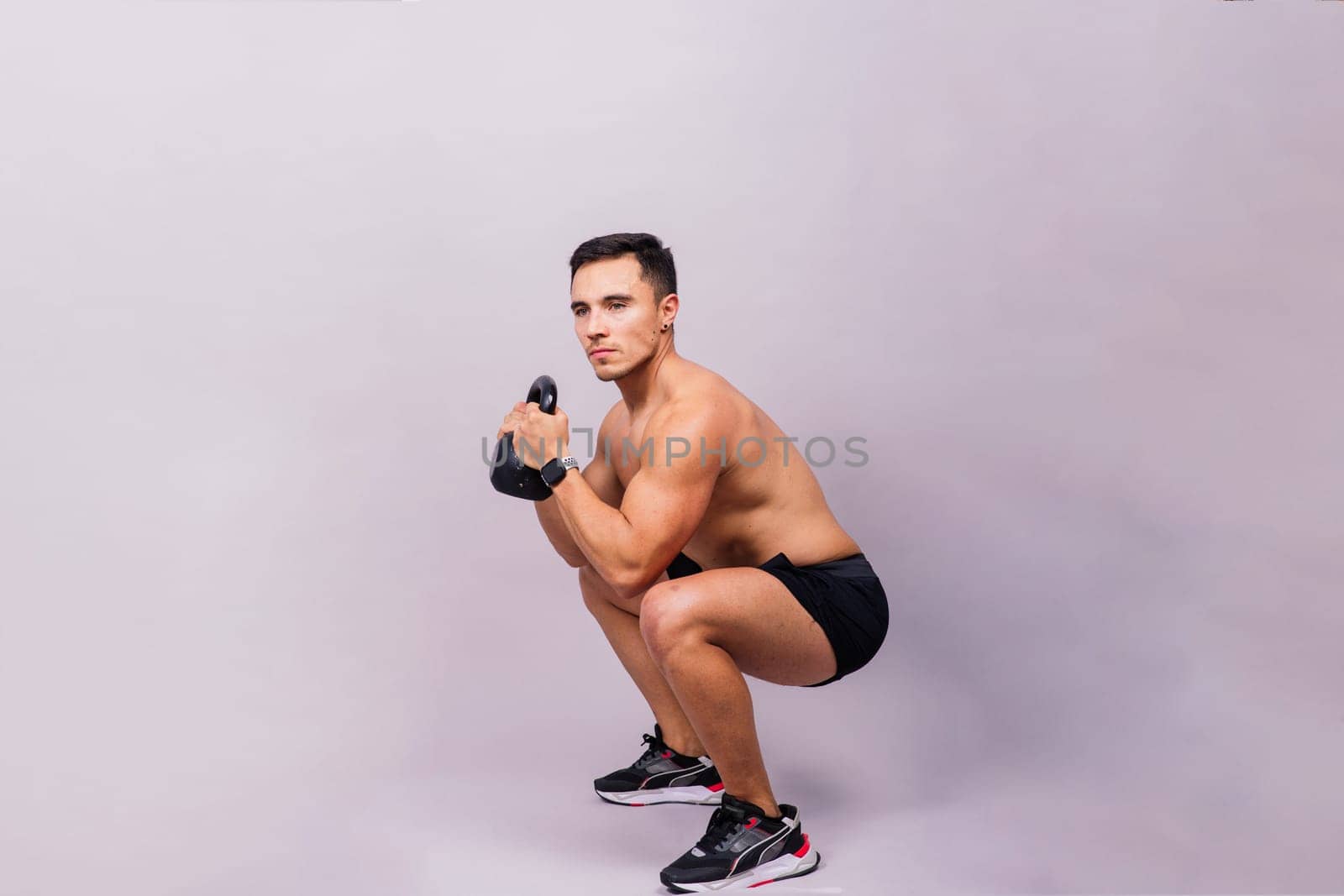 Hispanic male athlete working out with kettlebell on a grey background. Crossfit workout theme.