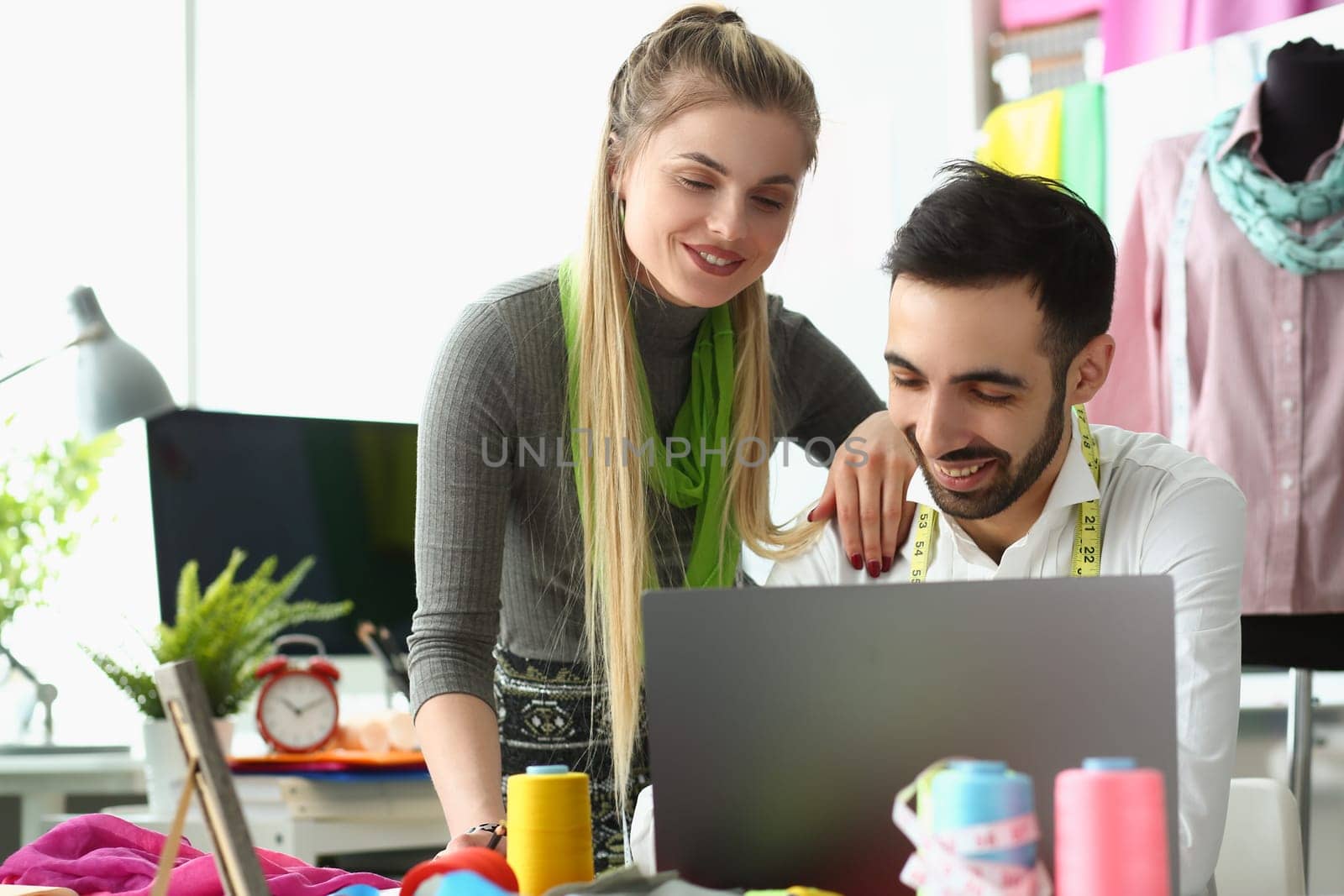 Young tailors work in atelier with laptop, creating fabric samples to create collection of clothes. Small business owners design team in sewing workshop