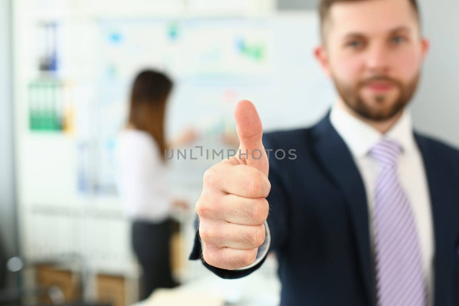 Businessman showing thumb up sign of success over blurred team of business people. Business consultant recommendation and successful career