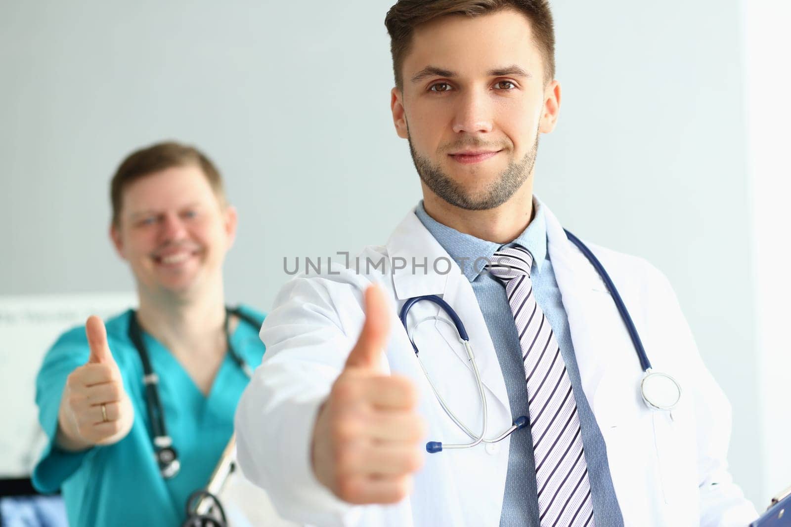 Two doctors gesture thumbs up in clinic recommending medical services by kuprevich
