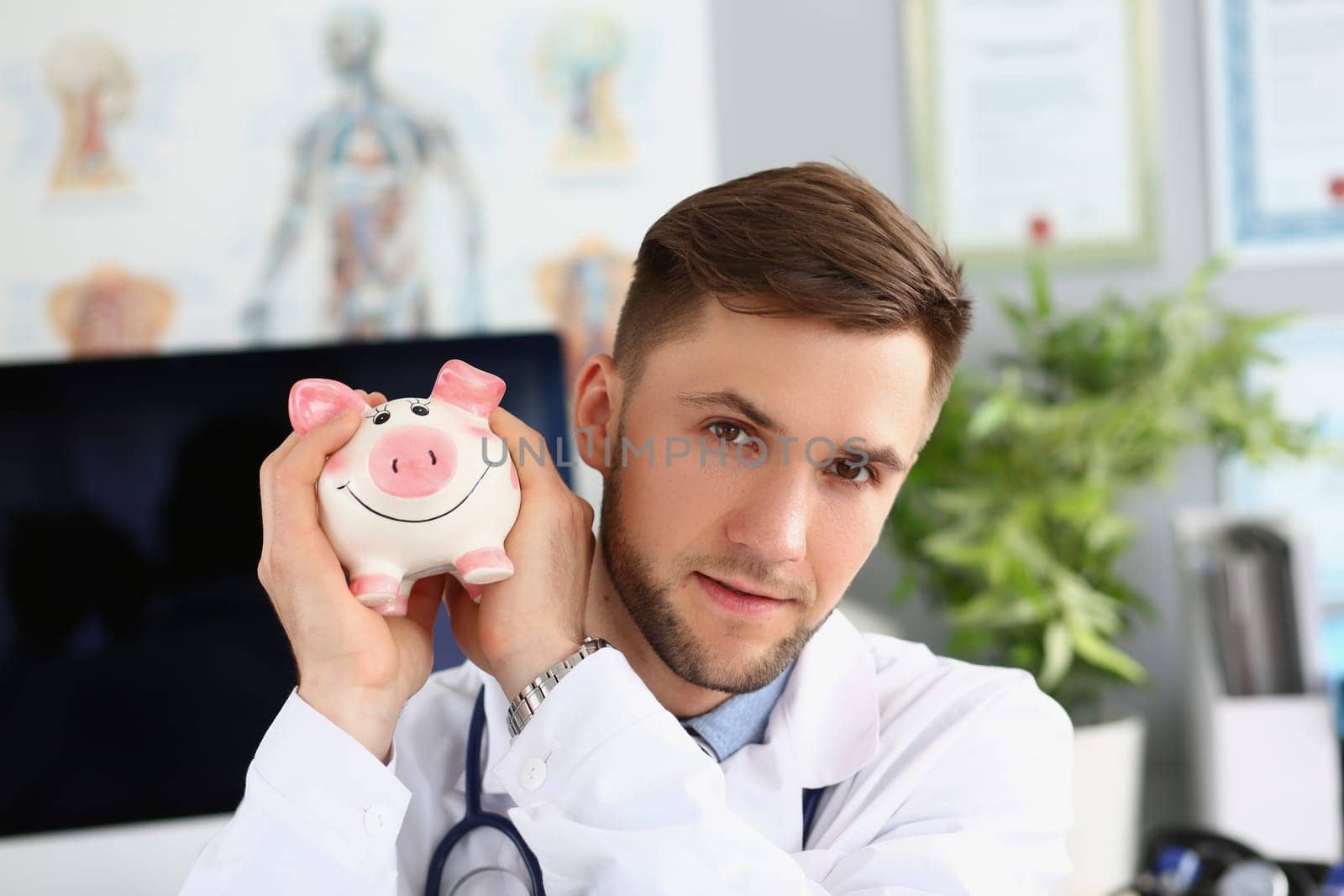 Portrait of male doctor holding a piggy bank on voluntary donations of money for a hospital or clinic. General practitioner collects charitable donation for patient care healthcare concept
