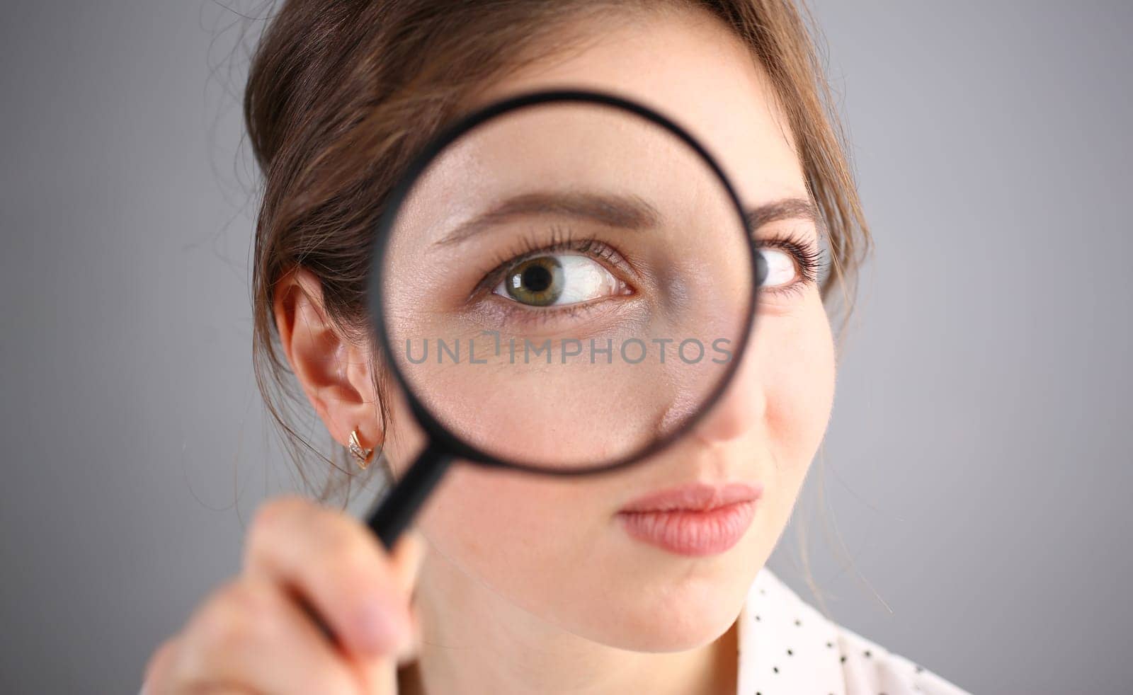 Inquisitive young woman looking through magnifying glass by kuprevich