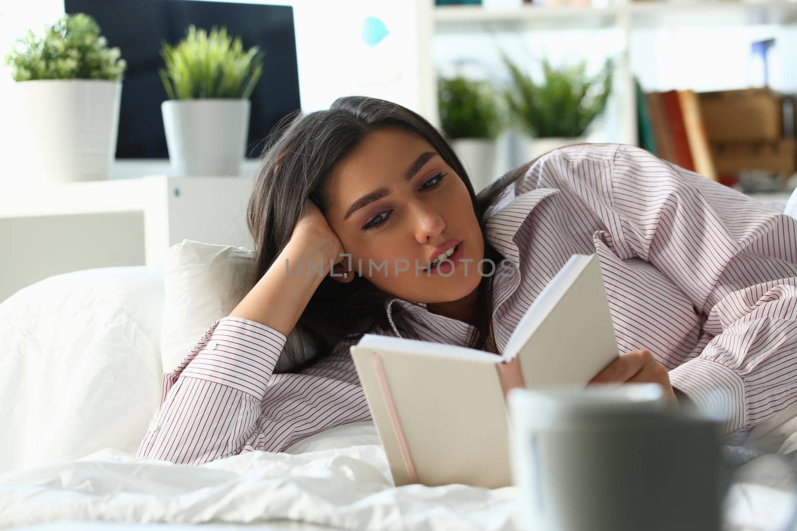 Beautiful woman lies in bed and reads book. Home leisure and reading novels