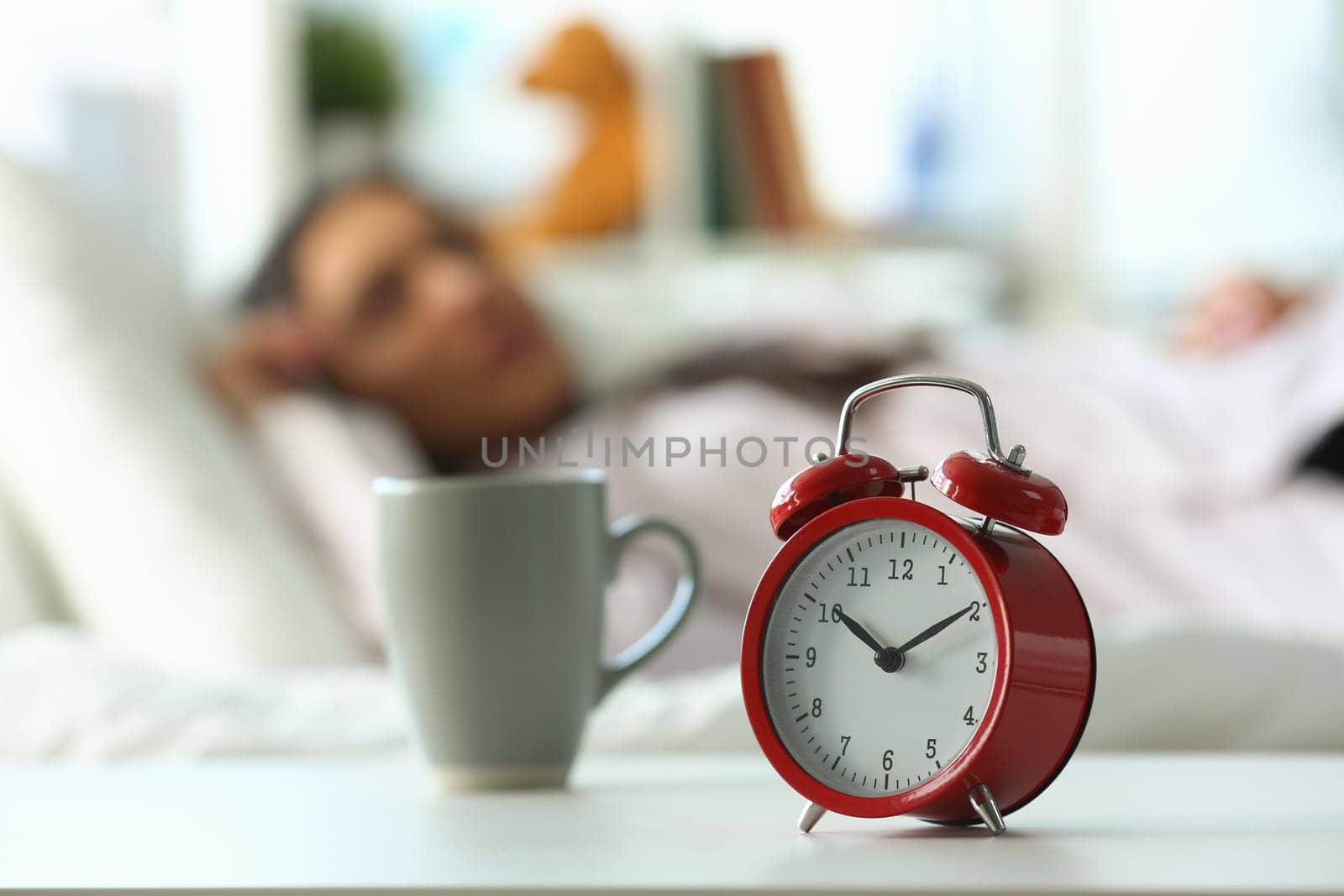 Red alarm clock at ten o'clock and sleeping woman. Peaceful sleep and late rise concept