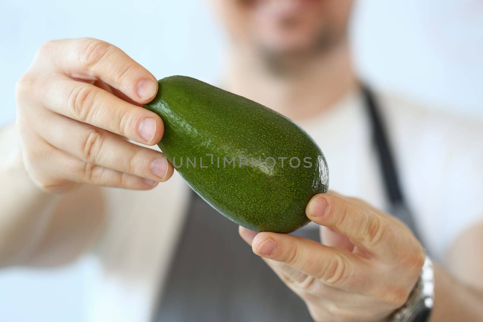 Male cook holds green fresh tasty avocado in hands. Natural fresh organic exotic fruits and healthy food concept