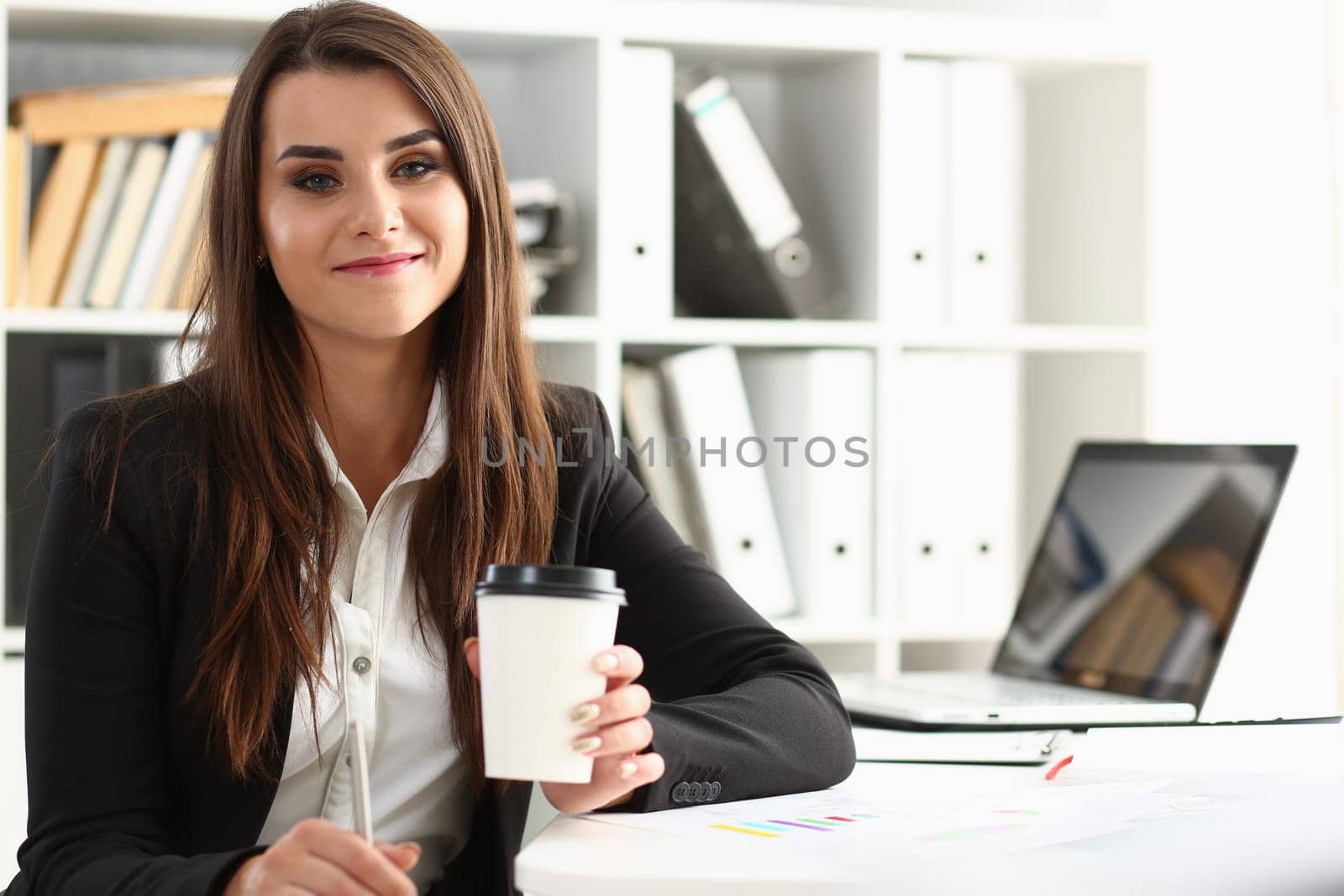 Beautiful young businesswoman holding glass of coffee at workplace by kuprevich
