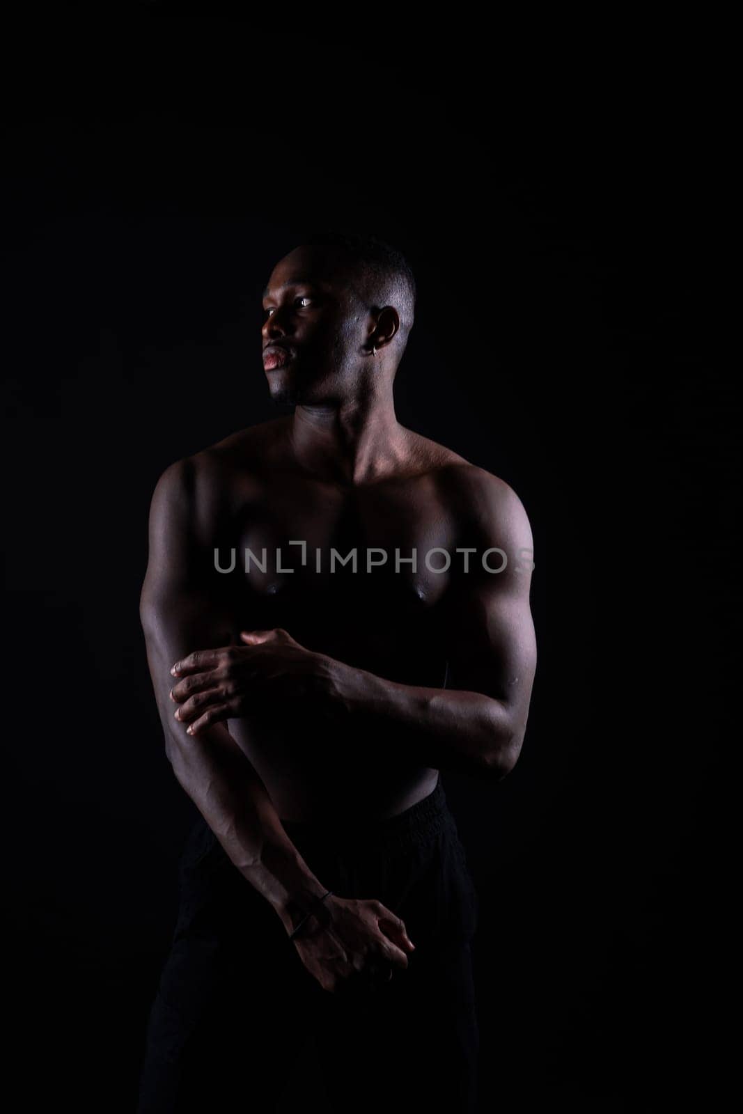 Athletic african american man topless, big muscles, a dark background studio