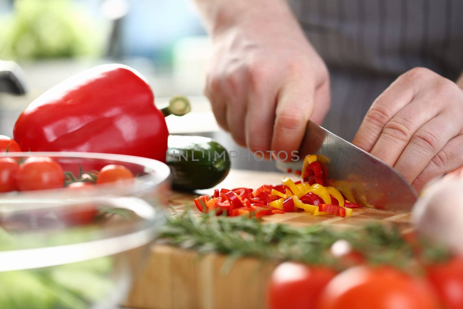 Hands of cook cut yellow and red peppers on cutting board with other vegetables on table in kitchen by kuprevich
