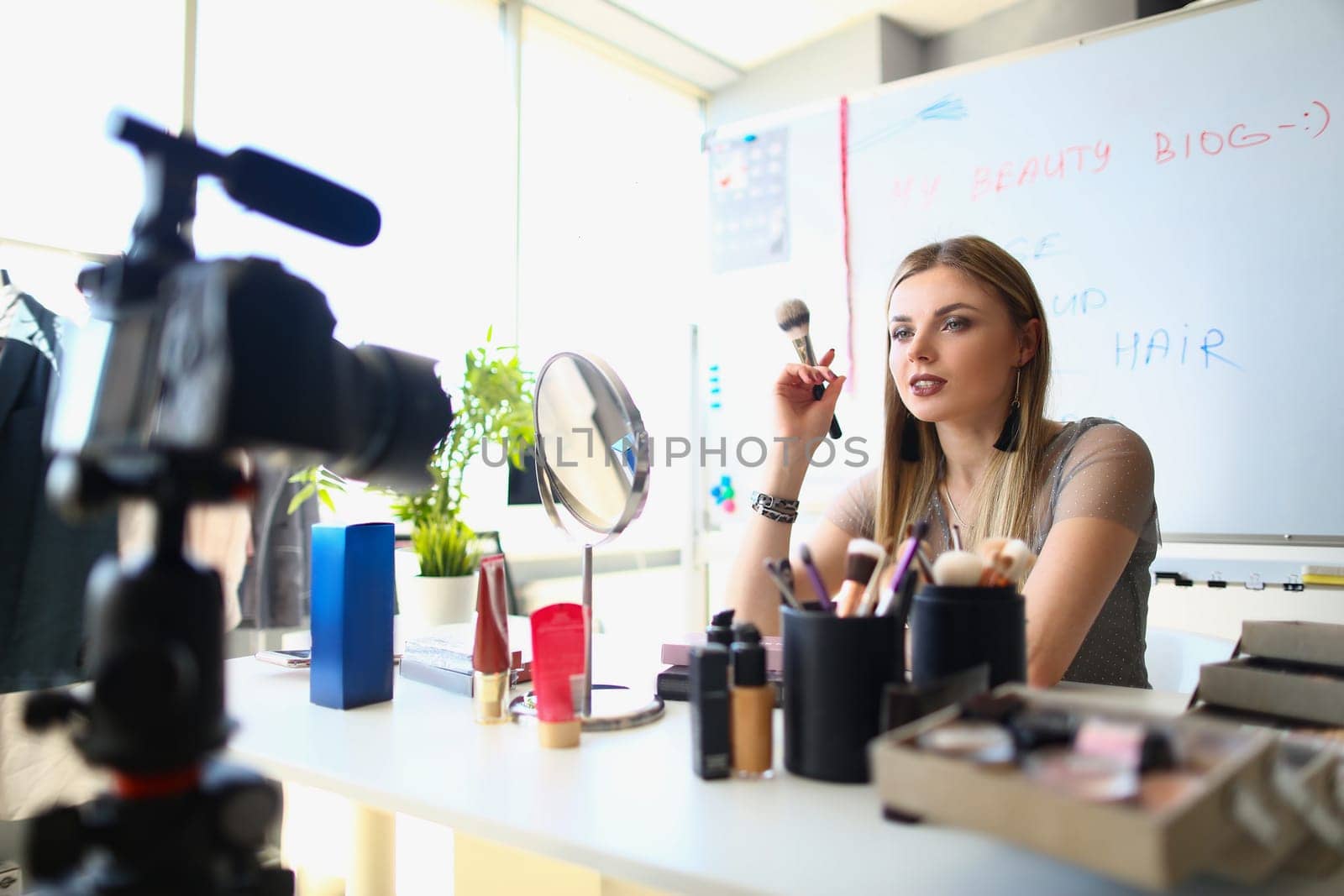 Woman talks about cosmetics with eye shadow blush palette and brushes recording online video. Woman blogger filming video for cosmetics blog