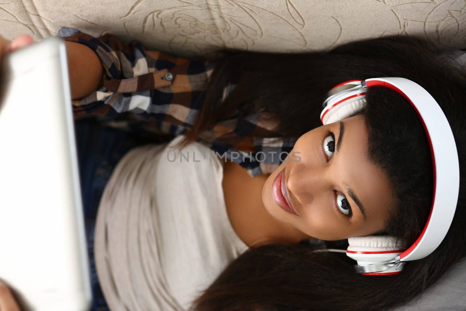 Portrait of a black woman in headphones working with laptop lying on couch at home top view by kuprevich