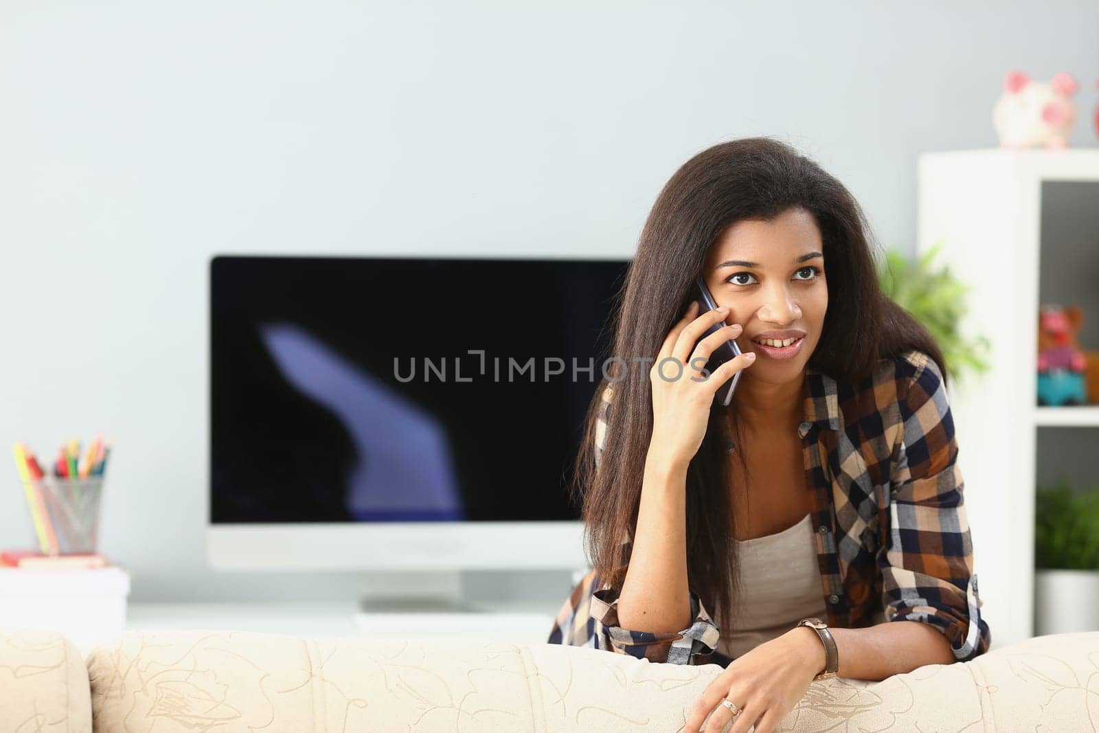 Cheerful young african american woman talking on smartphone, at home. Black woman calling and talking on phone with friend in living room concept