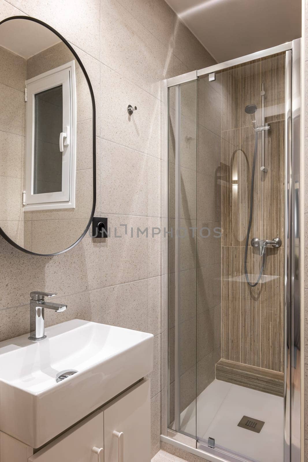 Comfortable compact bathroom with stylish beige tiles with glass shower, sink and modern shape mirror. Concept of a multifunctional bathroom in compact apartment by apavlin