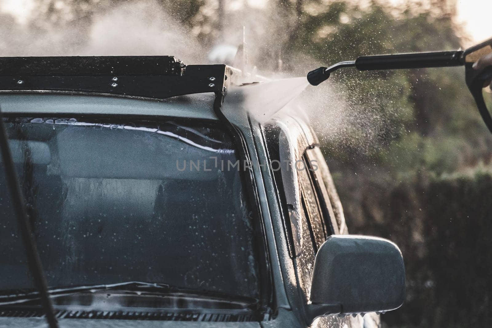 Close-up of washing car with high-pressure water hose on car wash service, splashing water around.