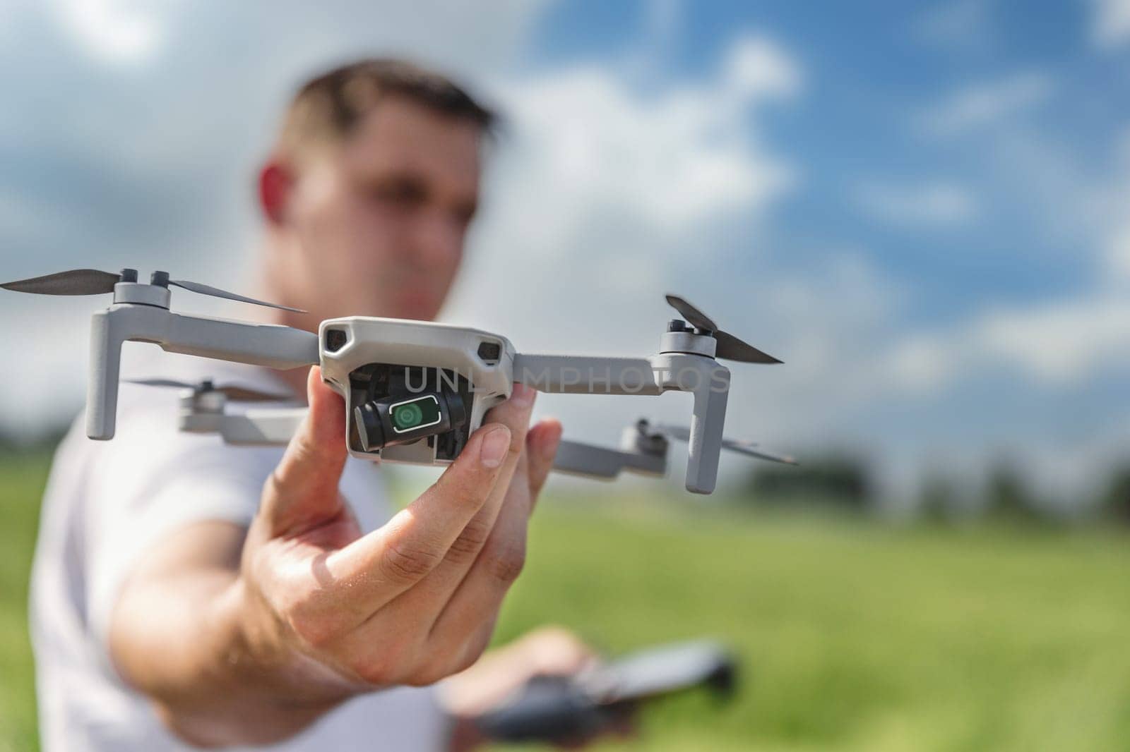 A quadcopter operator with a remote control out of focus holds a drone in front of him in focus outdoor.