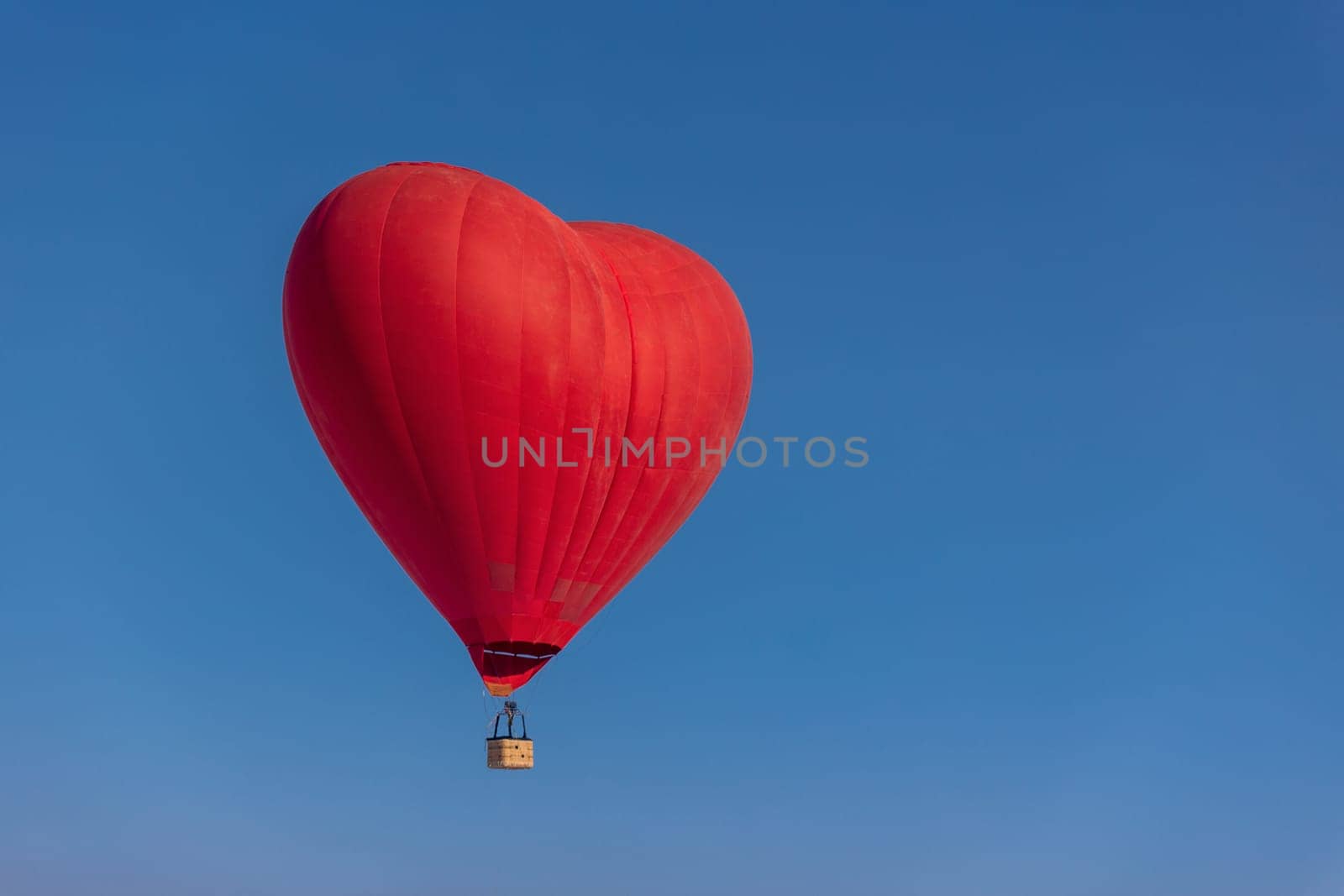 Hot air balloon in the shape of a heart in the blue sky. Honeymoon concept for newlyweds.