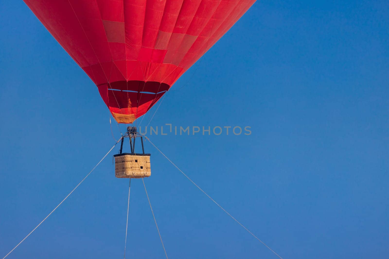 Empty basket from a red aerostat against a clear blue sky, copy space.
