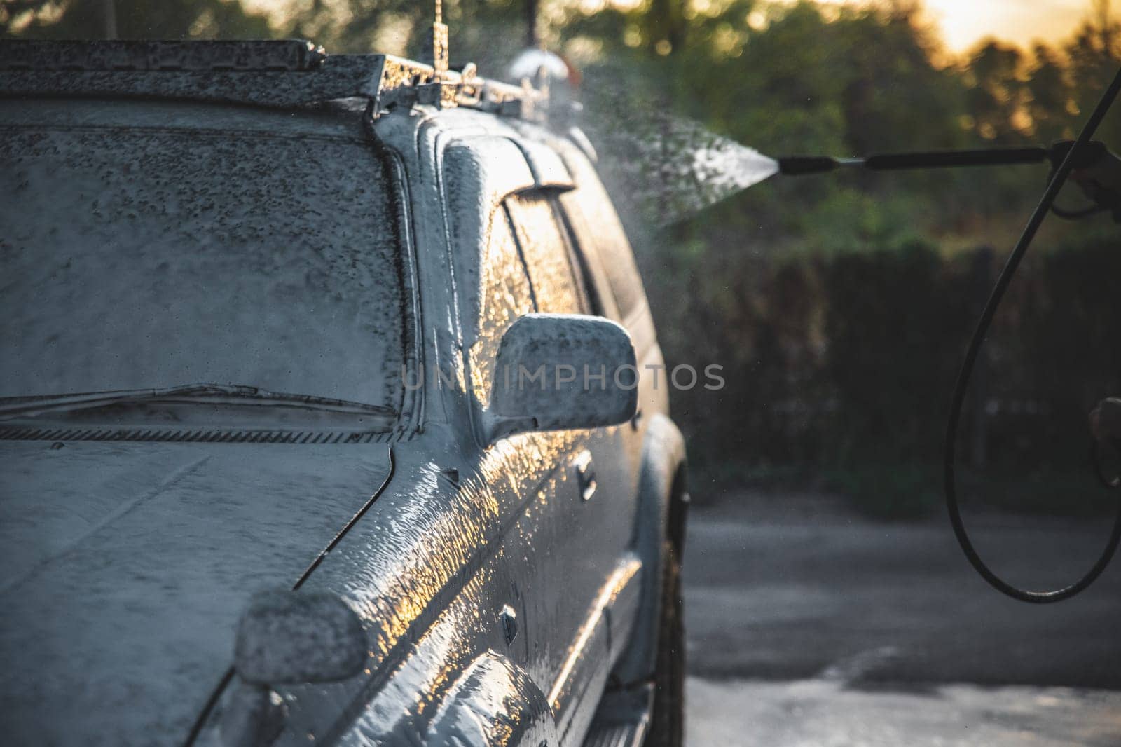 Treatment with white cleaning foam for washing a car from a high-pressure hose at a self-service car wash.