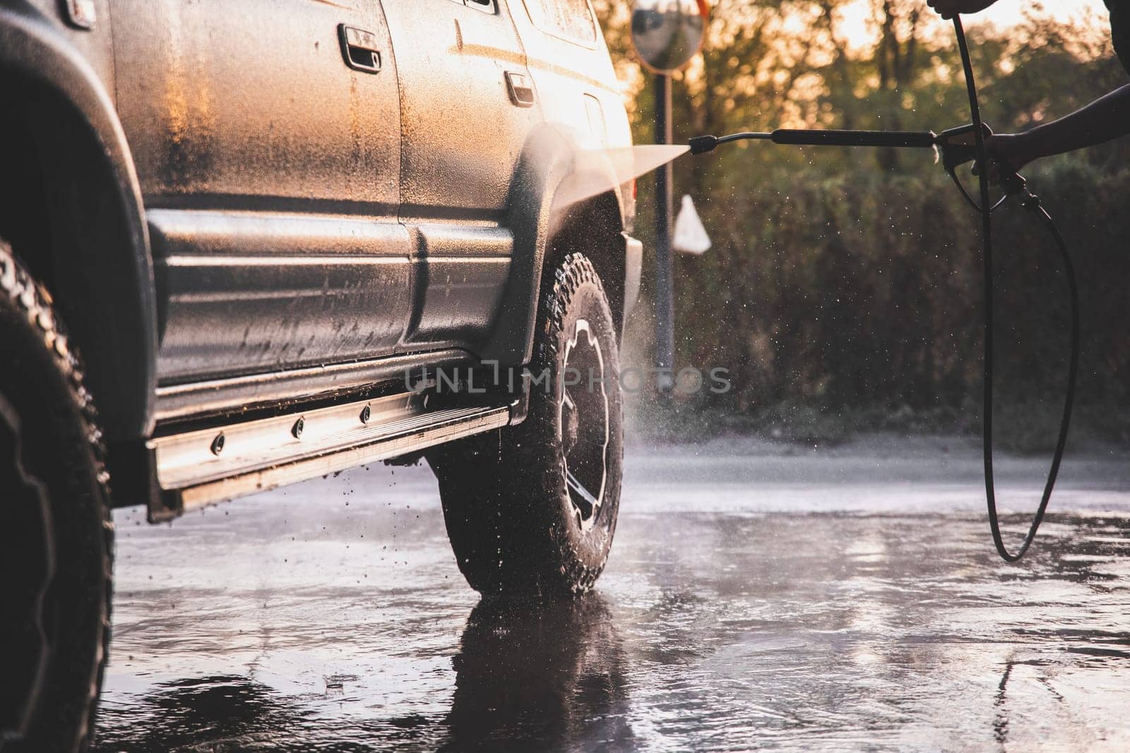 Washing SUV car at a self-service car wash with a high-pressure water jet after off-road driving.